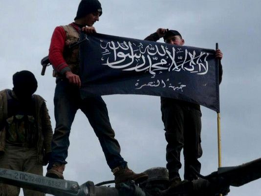 Syrian rebels waving an Al Qaeda flag over a government helicopter at a captured airbase.